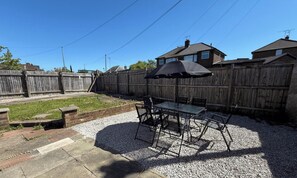 A backyard patio with a table and chairs, a covered umbrella, and a wooden fence.