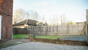Un giardino con una casa in mattoni, una recinzione di legno e un’area sterrata.