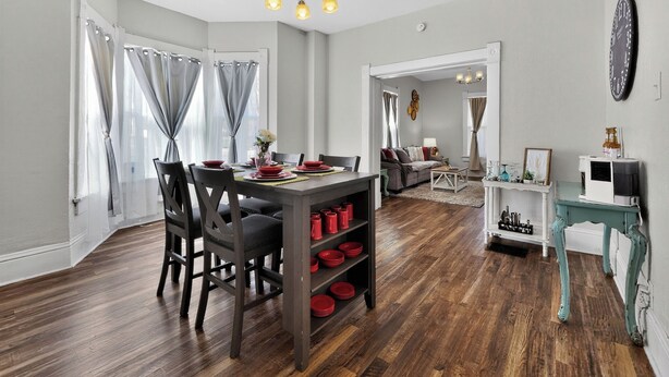 Un coin repas avec une table en bois, des chaises et un lustre. Il y a également un coin salon avec un canapé et une machine à café.