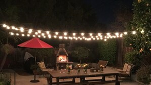 An outdoor patio with a wooden table and chairs, a red umbrella, and string lights. - 4-bedroom house in perfect Santa Barbara, 5 minutes from the beach! (Santa Barbara)