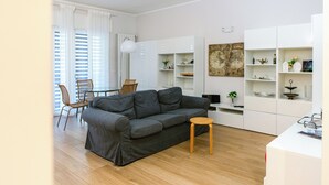 A modern living room with a grey sofa, wooden floor, white cabinets, and a dining area with chairs. - [Charm & Style Bari] Large Central Apartment (Bari)