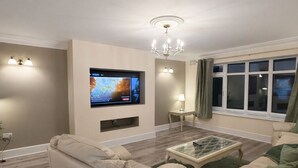 A modern living room with a flat-screen TV, two sofas, a glass coffee table, and a chandelier. - Beautifully Refurbished Home with 4 Bedrooms (Greenmount)