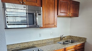 A kitchen with wooden cabinets, a stainless steel microwave, a double sink, and granite countertops. - 216 Panoramic Single Room in a waterfront hotel in Singer Island, FL (Riviera Beach)