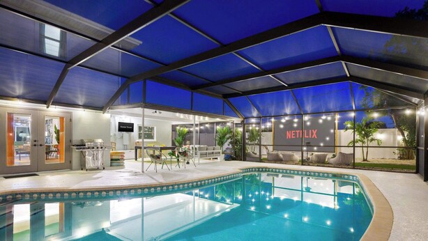 An indoor swimming pool with a Netflix sign, a covered seating area, and a bar. - Epic Backyard - Pool - Hot Tub - Outdoor Theatre (Bradenton)
