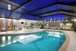 Une piscine intérieure avec un panneau Netflix, un espace détente couvert et un bar.