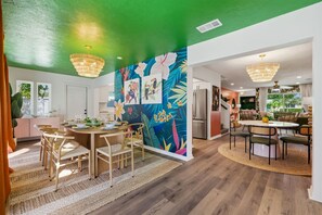 A modern kitchen with wooden cabinets, a dining area with a round table and chairs, and a vibrant tropical mural on the wall. - Epic Backyard - Pool - Hot Tub - Outdoor Theatre (Bradenton)