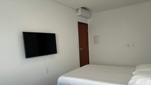 Una habitación de hotel con dos camas individuales, un televisor montado en la pared, un aire acondicionado y una puerta.