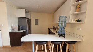 Una cuina moderna amb taulell blanc, un dispensador d'aigua, microones i nevera.