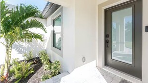 Een modern huis met een donkere voordeur, een klein raam en een verzorgde tuin met verschillende planten.