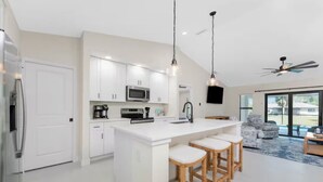 Een moderne keuken met witte kastjes, een centraal eiland met krukken, een magnetron en een koffiezetapparaat.