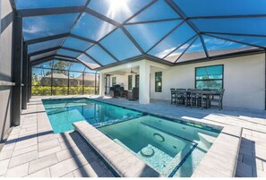 Un'area piscina moderna all'aperto con tetto in vetro, una zona relax separata con sedute e una vista libera sul paesaggio circostante.