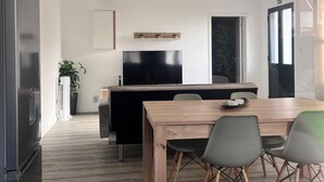 Ett modernt kök med matplats, TV och ett stort fönster med utsikt över elledningar.