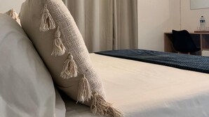 Ett hotellrum med en säng, beige gardiner, ett litet skrivbord med en stol och en spegel som hänger på väggen.