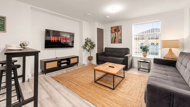 A modern living room with a flat-screen TV, a sofa, a coffee table, and a dining area with stools. - Central Manchester Haven | City Views | Sleeps 4 (Manchester)