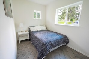 A bedroom with a bed, a nightstand, a lamp, and a window with a view of greenery.