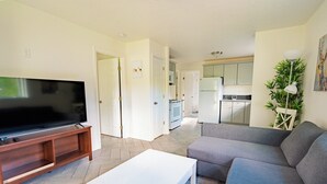Una sala de estar con un televisor de pantalla plana sobre un soporte de madera, un sofá gris y una mesa de centro blanca.