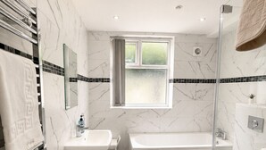 Une salle de bain moderne avec un mur en marbre, une baignoire, des toilettes et un espace douche.