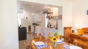 A dining area with a wooden table set for four, a vase of sunflowers, and a kitchen in the background. - Perfect 4-bedroom house with AC in pleasant Historic Bayside. (Northport)