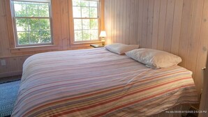 A bedroom with a bed, two windows, and a nightstand with a lamp. - Perfect 4-bedroom house with AC in pleasant Historic Bayside. (Northport)