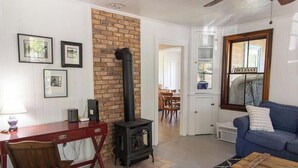 A cozy living room with a brick fireplace, a dining area with a table and chairs, and a blue sofa. - Perfect 4-bedroom house with AC in pleasant Historic Bayside. (Northport)