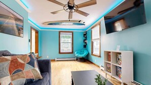 Quarto com ventilador de teto, poltrona de encosto, estante de livros e planta em vaso.