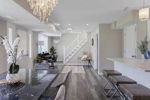 A modern kitchen with a central island, a dining area with a chandelier, and a staircase leading to an upper level.