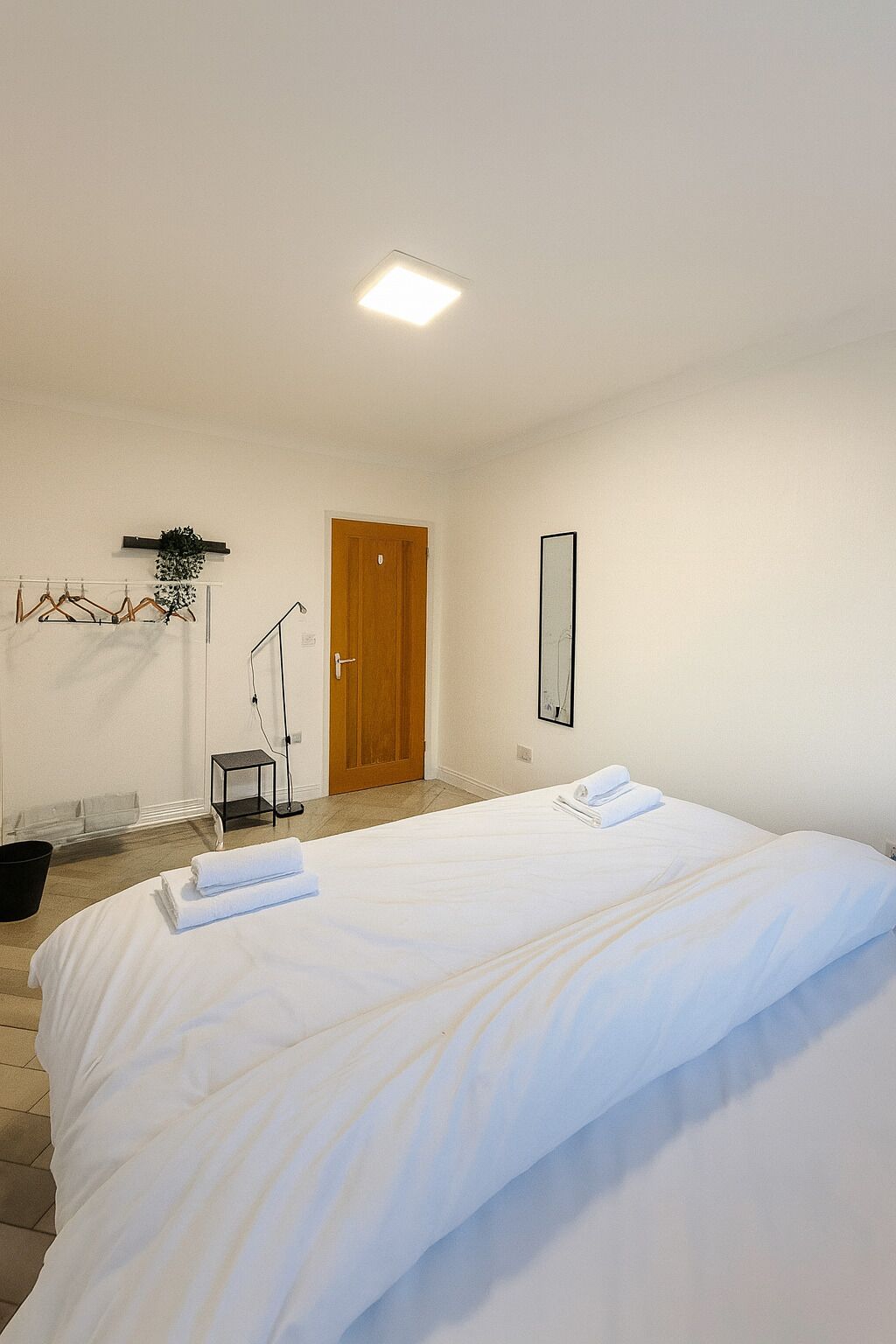Hotellihuone, jossa on suuri sänky, puuovi, peili ja pieni pöytä, jonka päällä on kasvi.