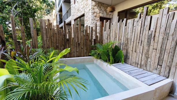 A rectangular pool with a wooden deck, surrounded by lush tropical plants and a rustic wooden fence. - Luxury Apartment in Tulum - Private Pool - Sleeps 8 (Tulum)
