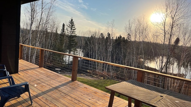 A wooden deck with a table and chairs, overlooking a body of water and trees. - Chalet 14 pers | Motoneige & Nature | Près du Valinouët - Monts Valin (Saint-David-de-Falardeau)