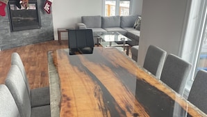 A conference room with a large wooden table, grey upholstered chairs, a grey sofa, and a fireplace with stockings. - Chalet 14 pers | Motoneige & Nature | Près du Valinouët - Monts Valin (Saint-David-de-Falardeau)