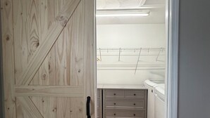 Quarto com porta de madeira, um armário branco com gavetas e uma cama com cabeceira branca.