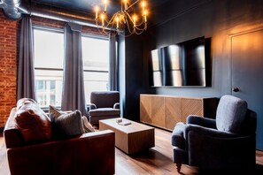 Ein modernes Wohnzimmer mit einer Ledersofa, einem grauen Sessel, einem Holztisch und einem großen Flachbildfernseher an der Wand.