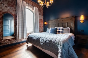 A bedroom with a large bed, a wooden headboard, a brick wall, and a window with curtains. - The Blue Hour Suite (Louisville)
