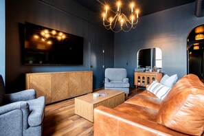 A modern living room with a large flat-screen TV, a leather sofa, a wooden coffee table, and a grey armchair. - Hollyhock Suite 401: 4 bed/2 bath with soaking tub (Louisville)