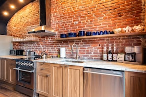 A kitchen with a brick wall, stainless steel appliances, and a coffee machine. - The Blue Hour Suite (Louisville)