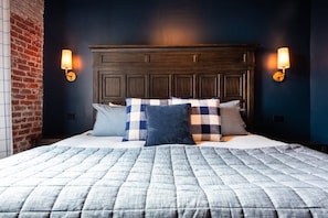 Une chambre avec un grand lit, une tête de lit sombre et deux lampes fixées au mur.