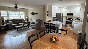Una cocina moderna con armarios blancos, una mesa de comedor con sillas y una sala de estar con sofá y sillones.