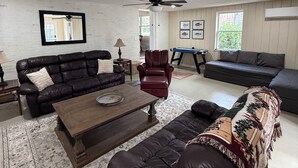 Una sala de estar con un sofá de cuero marrón, un sillón de cuero rojo, una mesa de centro de madera y una alfombra estampada.
