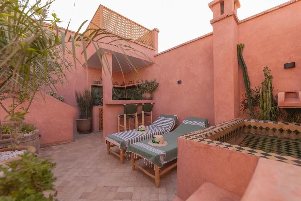 A cozy outdoor seating area with two lounge chairs and a small table, surrounded by potted plants and a decorative wall.
