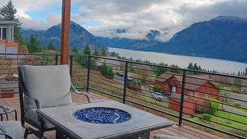 Un balcon avec coin salon extérieur, un foyer et une vue sur les montagnes et un lac.