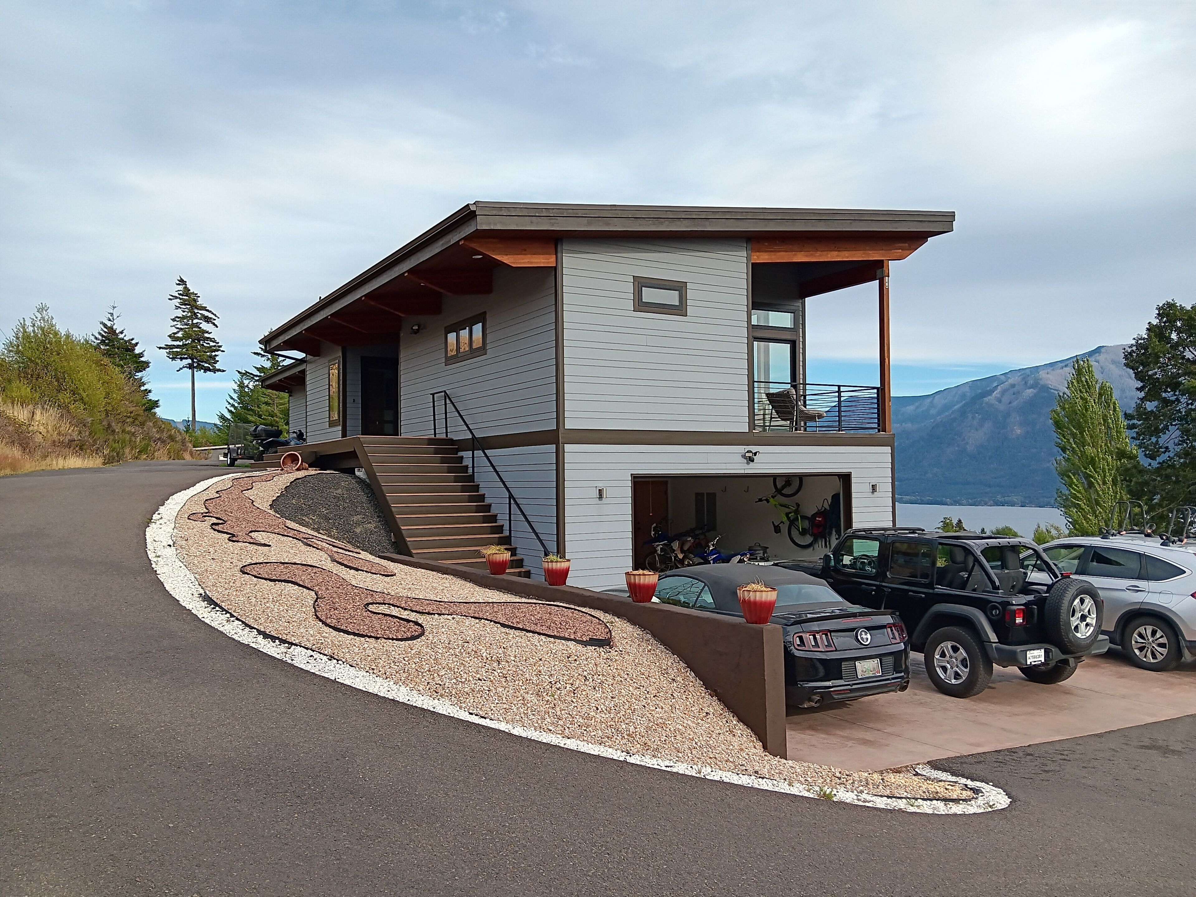Une maison moderne à deux étages, dotée d’un garage, d’une allée décorative et offrant une vue sur les montagnes.