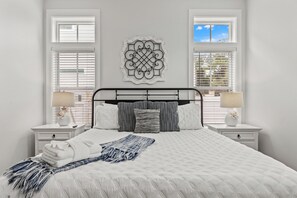 Ein Schlafzimmer mit einem großen Bett, zwei Nachttischen, einer Wanddekoration und einem Fenster mit Jalousien.