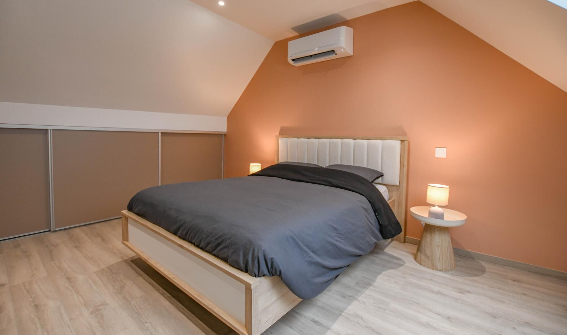 A modern bedroom with a bed, two bedside lamps, and an air conditioning unit.