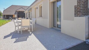A modern building with a patio area featuring a table and chairs, a brick wall, and a sliding glass door. - Le Petit Chez Thérèse - FONTAINE LES GRES (FONTAINE LES GRES)