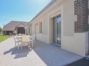 Un bâtiment moderne doté d’un patio comprenant une table et des chaises, un mur en briques et une porte-fenêtre coulissante.