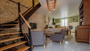 Una sala de estar moderna con pared de piedra, una escalera de madera, un sofá y un comedor.