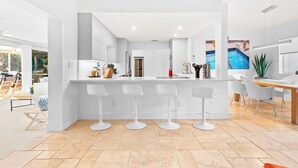 A modern kitchen with white cabinetry, a central island with bar stools, and a dining area with a wooden table and chairs. - Intervillas Florida - Villa Barracuda (Cape Coral)