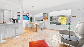 A modern kitchen with white cabinetry, a dining area with a table and chairs, and a living area with a sofa and a small round table. - Intervillas Florida - Villa Barracuda (Cape Coral)