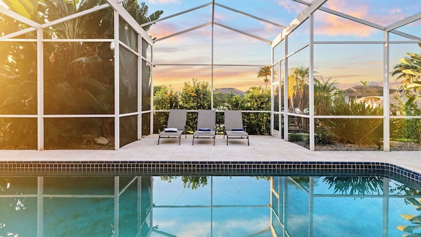 A pool area with a glass enclosure, three lounge chairs, and a view of the surrounding landscape. - Intervillas Florida - Villa Barracuda (Cape Coral)
