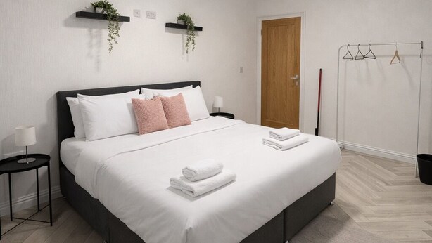 Une chambre moderne avec un grand lit, des tables de chevet, une porte en bois et un portant à vêtements.